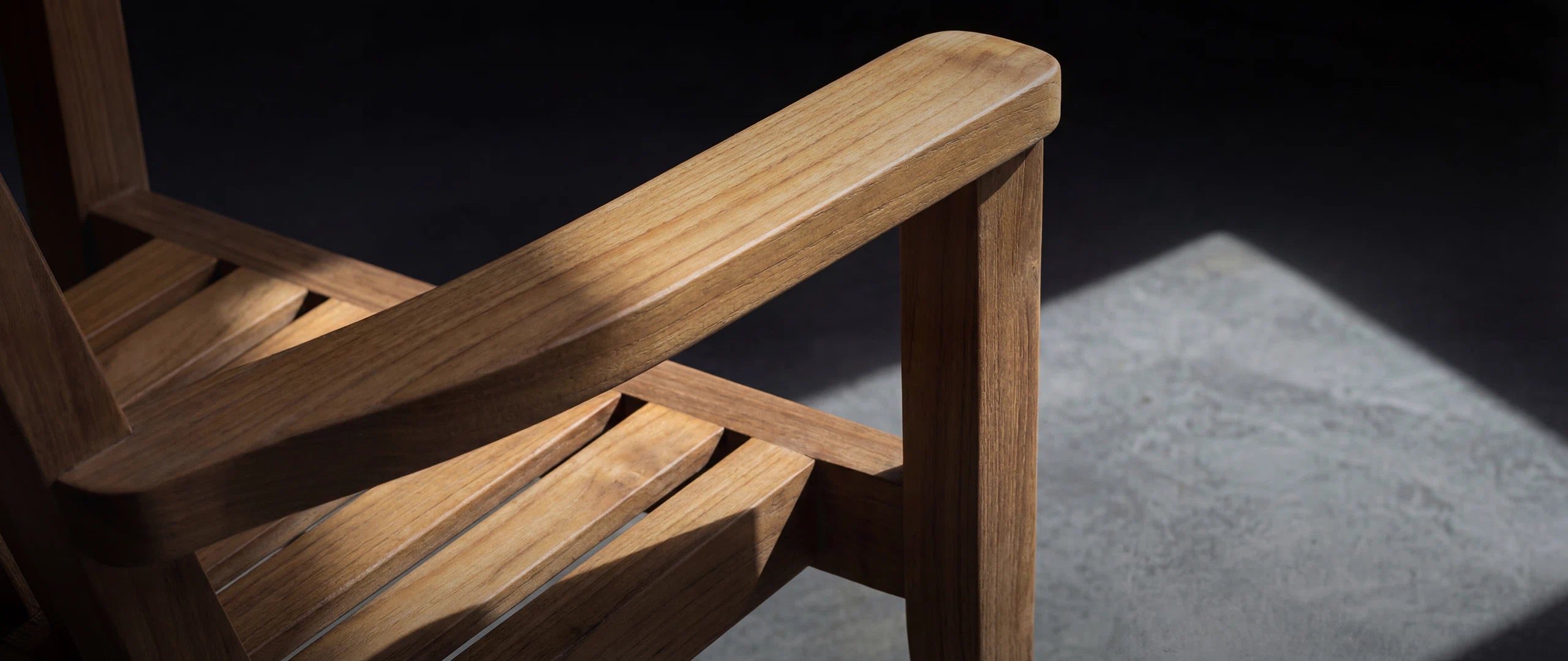 Detailaufnahme eines exklusiven Menelamé Outdoor-Sessels aus massivem Teakholz. Die ergonomische Armlehne unterstreicht die Verbindung von höchster Handwerkskunst und modernem Design.