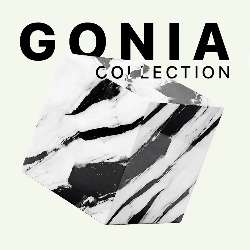 Werbeaufnahme der Gonia Collection von Menelame. Zu sehen ist der monolithische Beistelltisch aus Panda White Marmor mit seiner markanten, kontrastreichen schwarz-weißen Maserung vor dem Markenschriftzug.