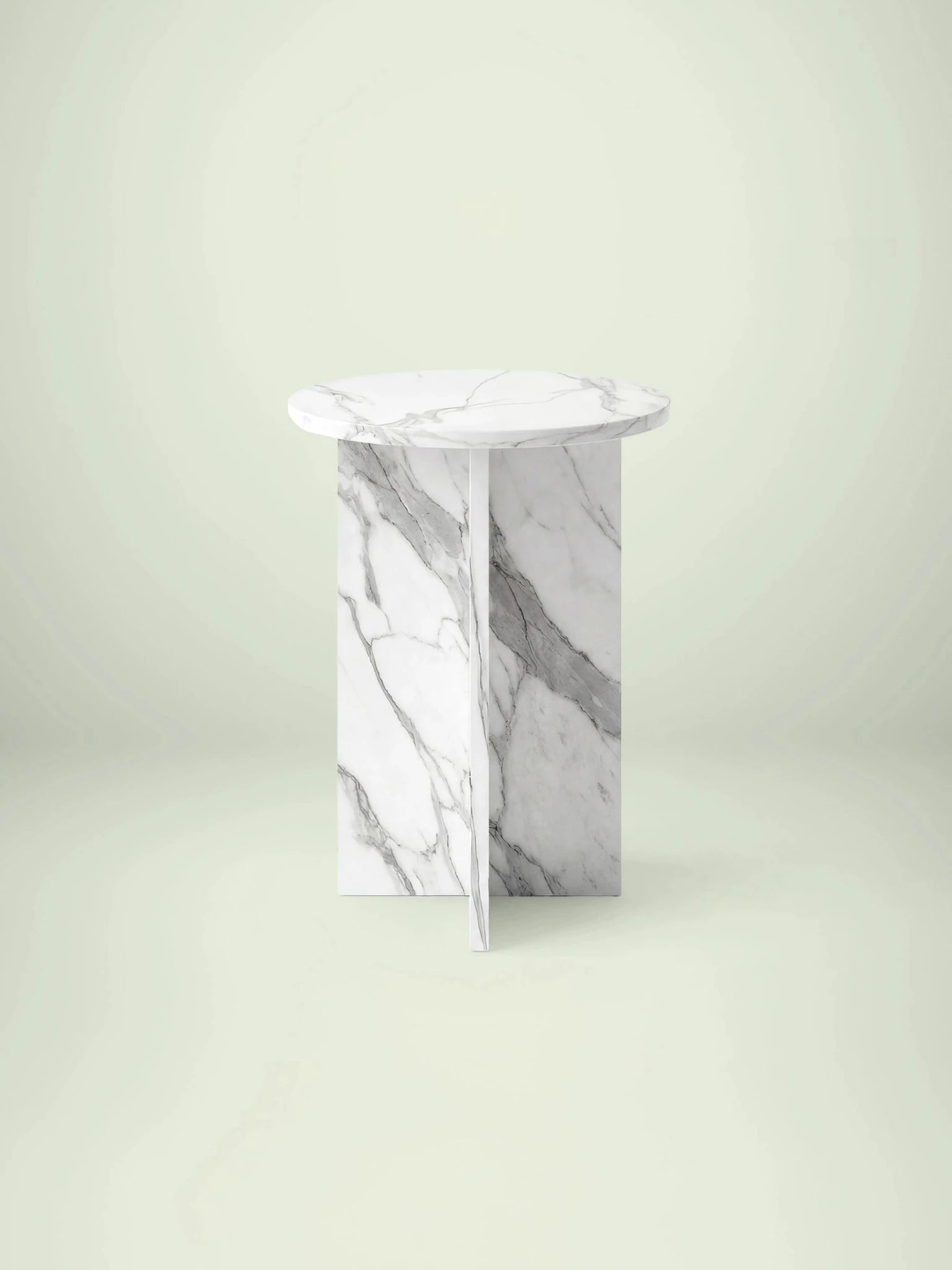 Frontalansicht des runden Beistelltischs Hillu aus Calacatta White Marmor mit skulpturalem, kreuzförmigem Untergestell.