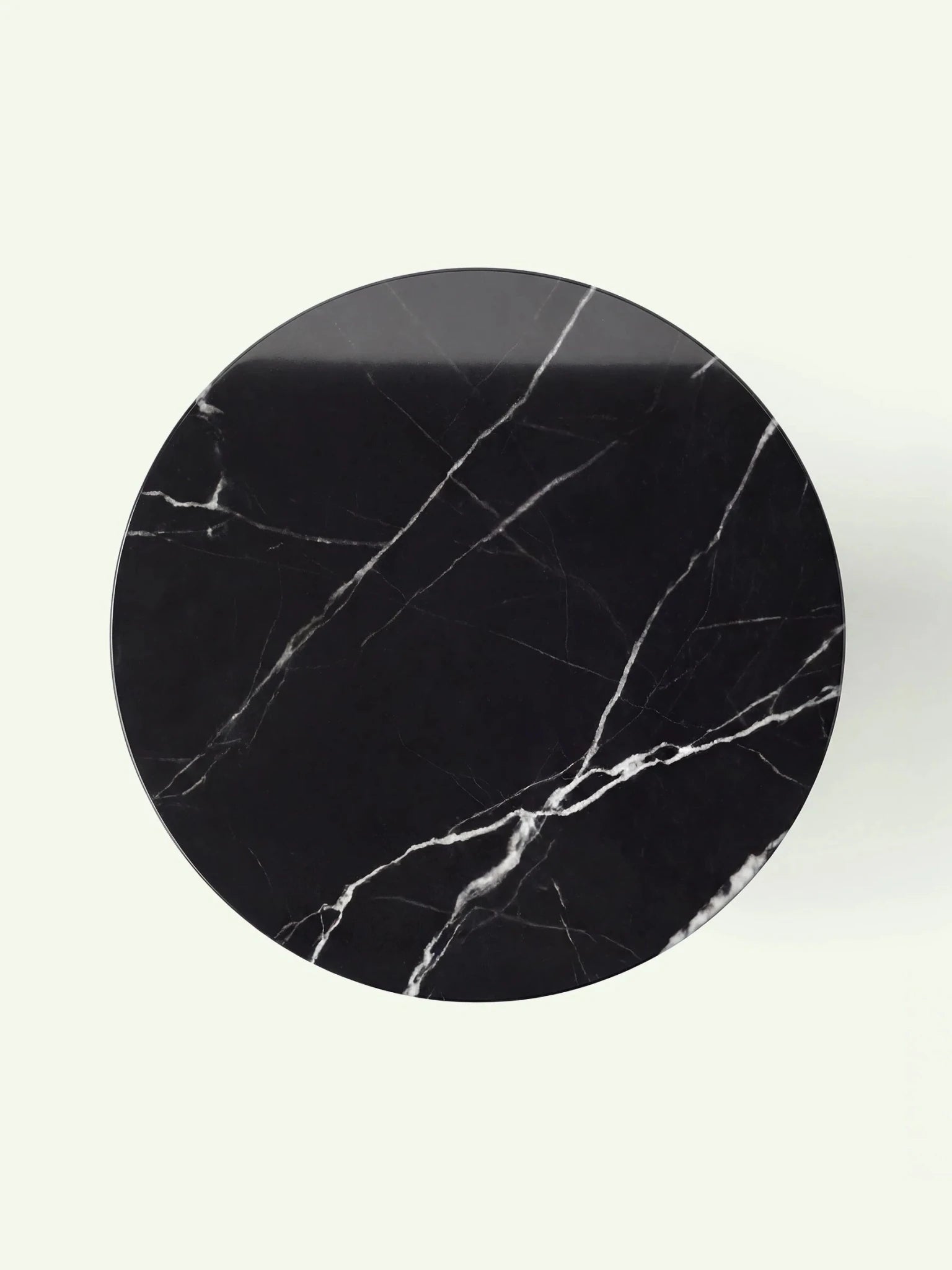 Blick von oben auf die runde Tischplatte des Modells Hillu aus Nero Marquina Marmor mit markanten weißen Adern.