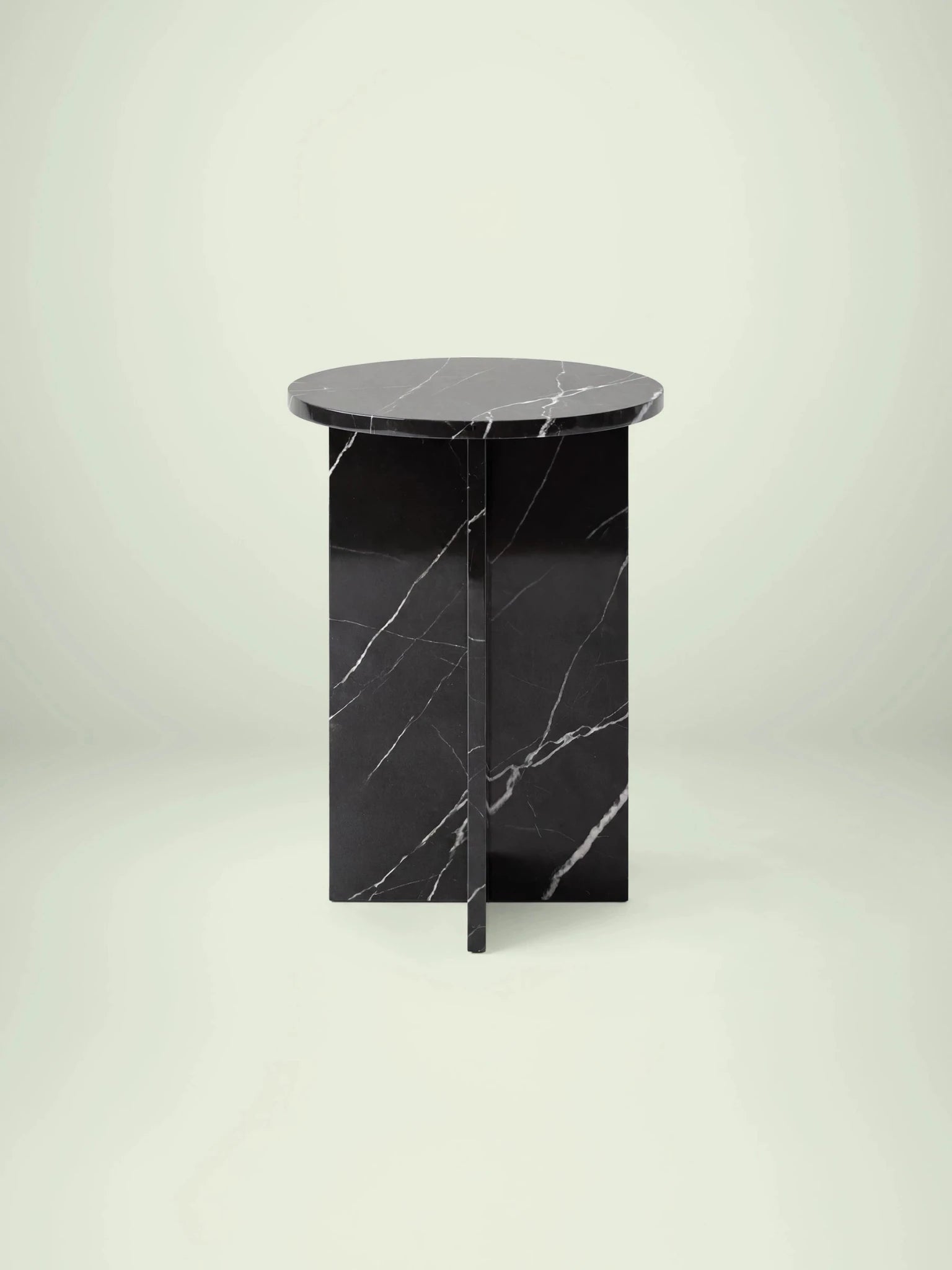 Frontalansicht des Marmor-Beistelltischs Hillu mit runder Platte und kreuzförmigem Untergestell aus Nero Marquina Marmor.