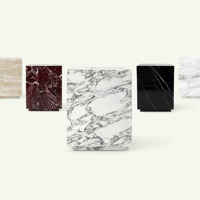 Kollektionsübersicht der Pella Beistelltisch-Serie. Im Vordergrund steht das Modell aus Arabescato Marmor, flankiert von den Varianten in Rosso Levante, Nero Marquina, beigem Travertin und Calacatta White.