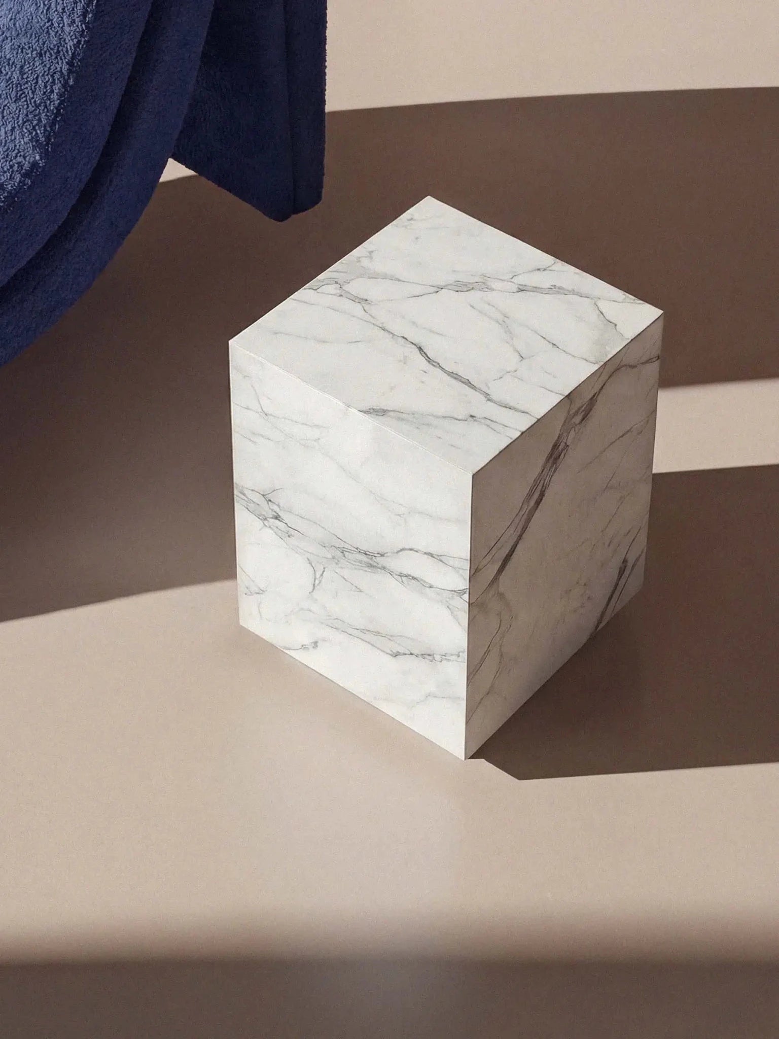 Lifestyle-Aufnahme des Marmortischs Pella von oben, die die elegante graue Äderung des Calacatta White Marmors im Sonnenlicht zeigt.