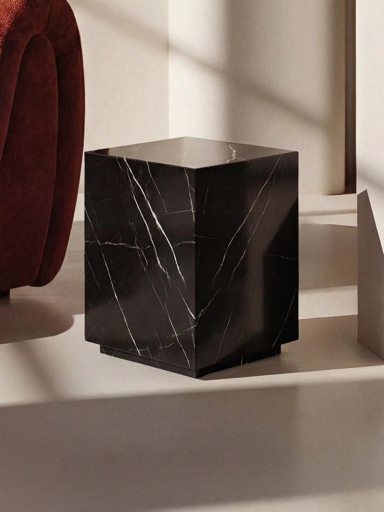 Der schwarze Marmor-Beistelltisch Pella in einer eleganten Raumsituation mit weichem Lichteinfall neben einem roten Polstermöbel.