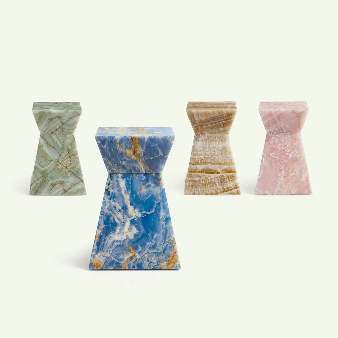 Kollektionsübersicht der Suela Beistelltische aus Onyx. Im Vordergrund steht das Modell in Blue Onyx, flankiert von den Varianten in grünem Onyx, Honig-Onyx und Rose-Onyx, was die natürliche Farbvielfalt der Serie verdeutlicht.