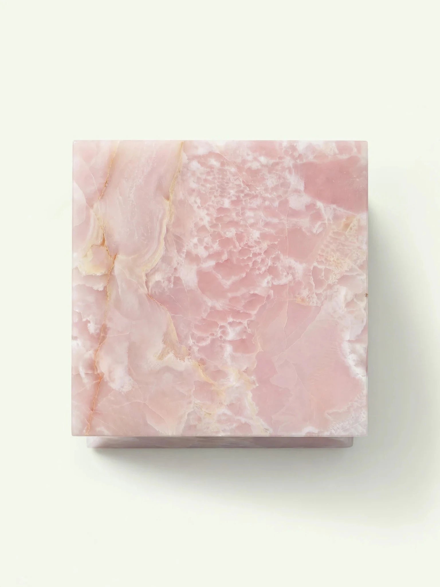 Blick von oben auf die quadratische Tischplatte des Suela Beistelltischs mit der feinen, wolkenartigen Maserung des rosa Onyx