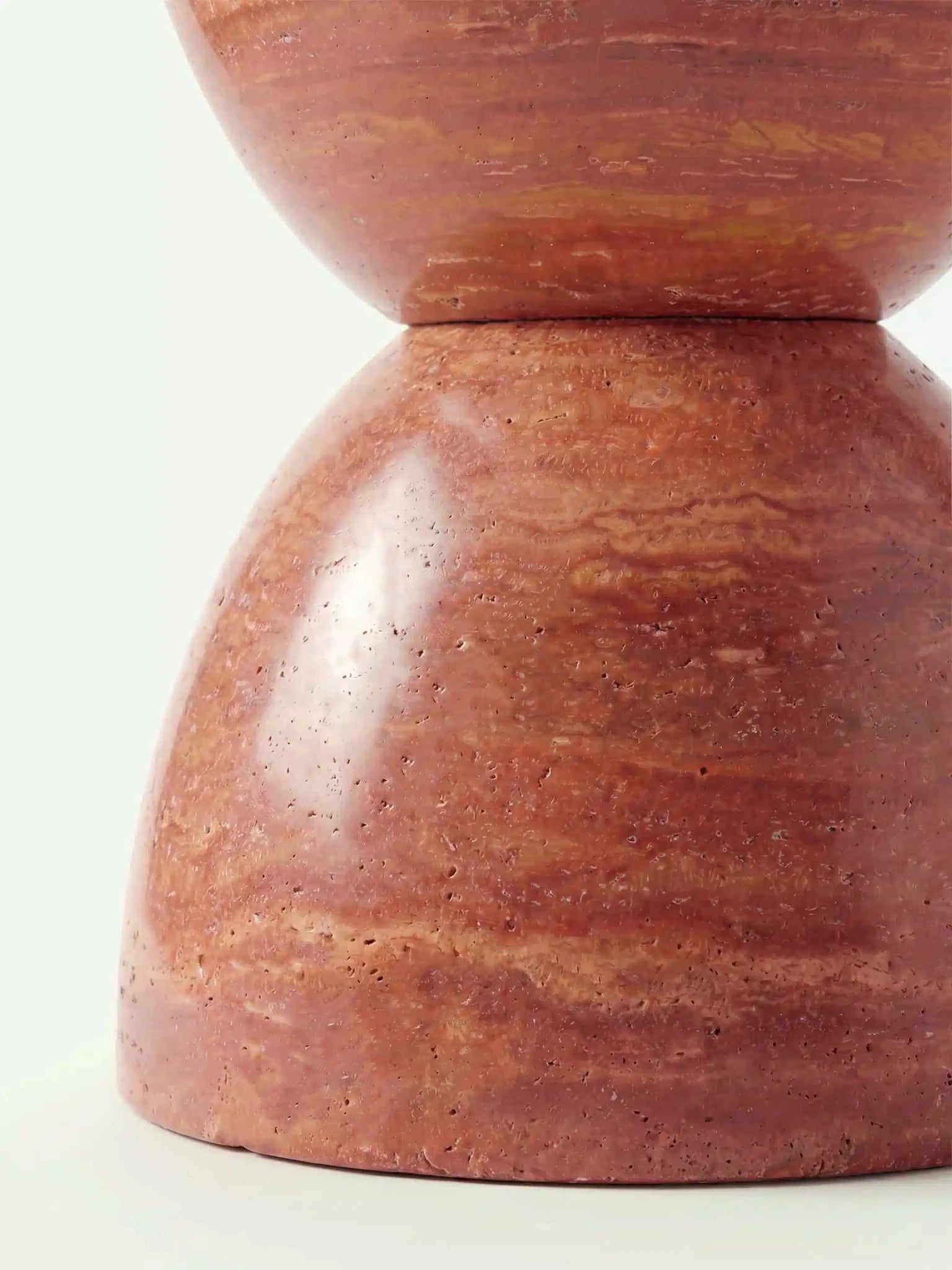 Detailaufnahme der bauchigen Basis des Modells Kromi aus rotem Travertin, die die polierte Oberfläche und die natürliche Steinstruktur zeigt.