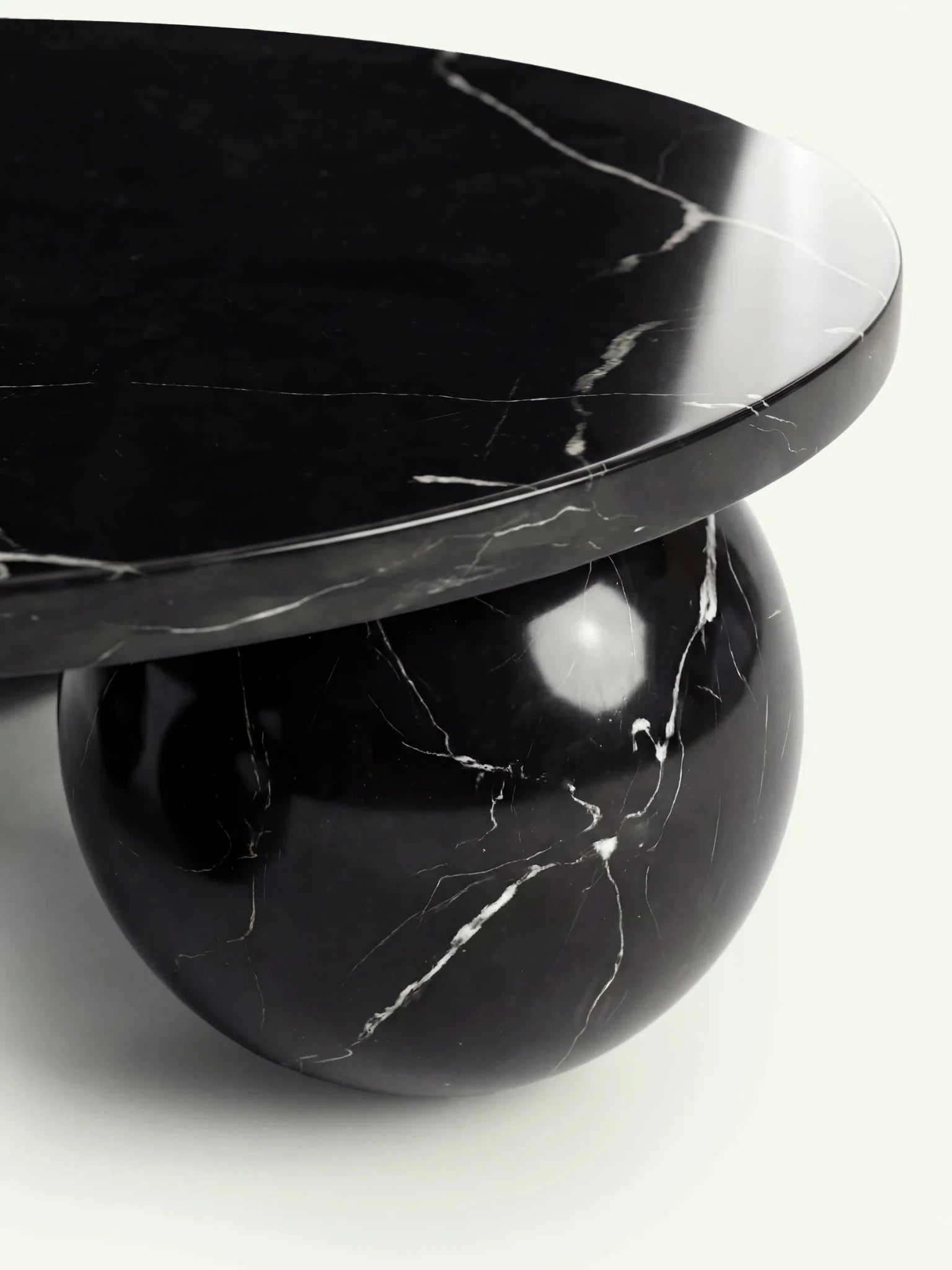 Detailaufnahme einer der stützenden Kugelfüße des Belnor Couchtischs. Die Nahaufnahme zeigt die polierte Oberfläche des Nero Marquina Marmors mit seinen charakteristischen, feinen weißen Kalkadern.