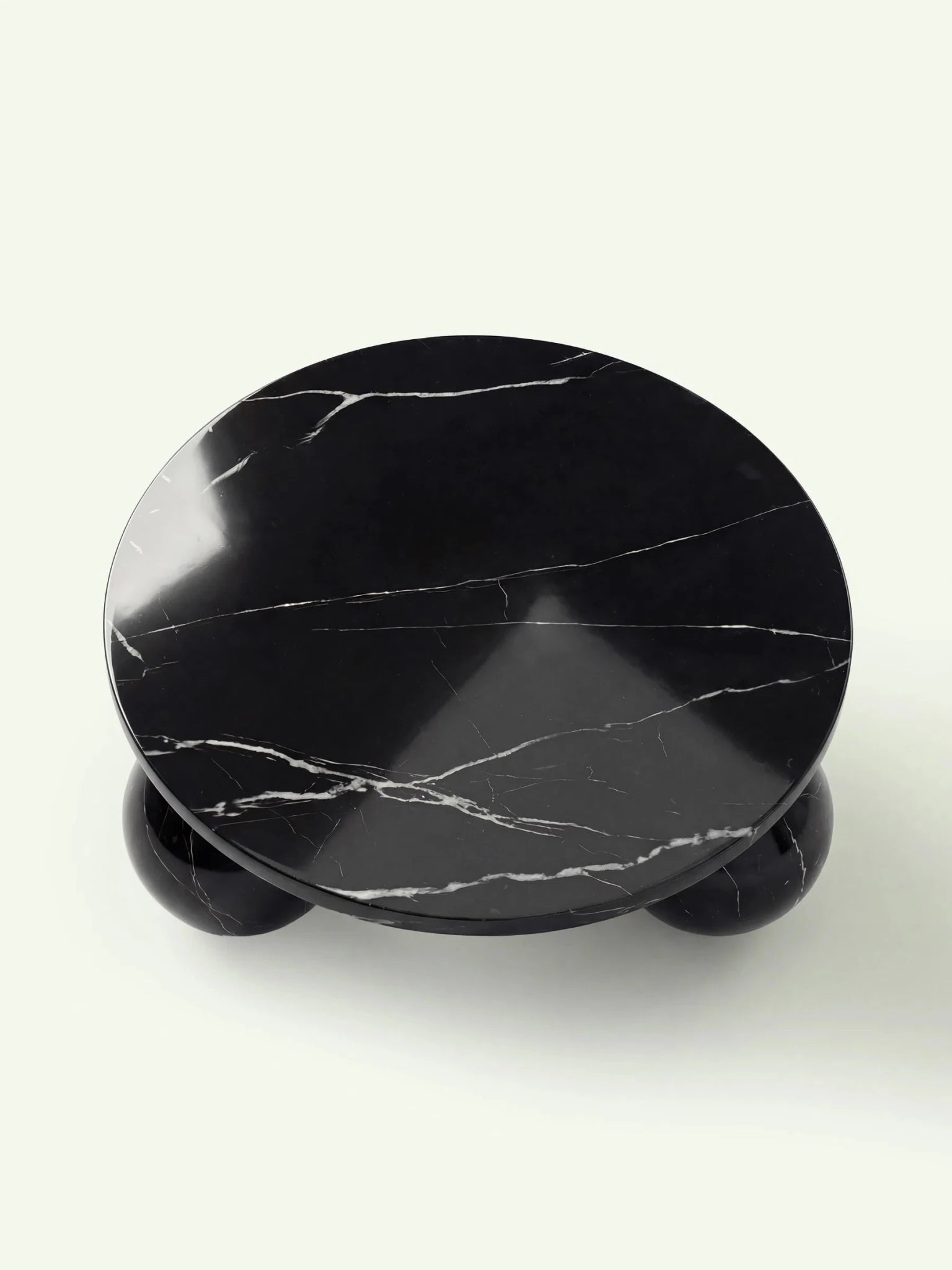 Draufsicht auf den Belnor Couchtisch aus Nero Marquina Marmor. Die Vogelperspektive zeigt die kreisrunde Tischplatte und die markante natürliche Zeichnung des schwarzen Marmors mit horizontal verlaufenden weißen Adern.