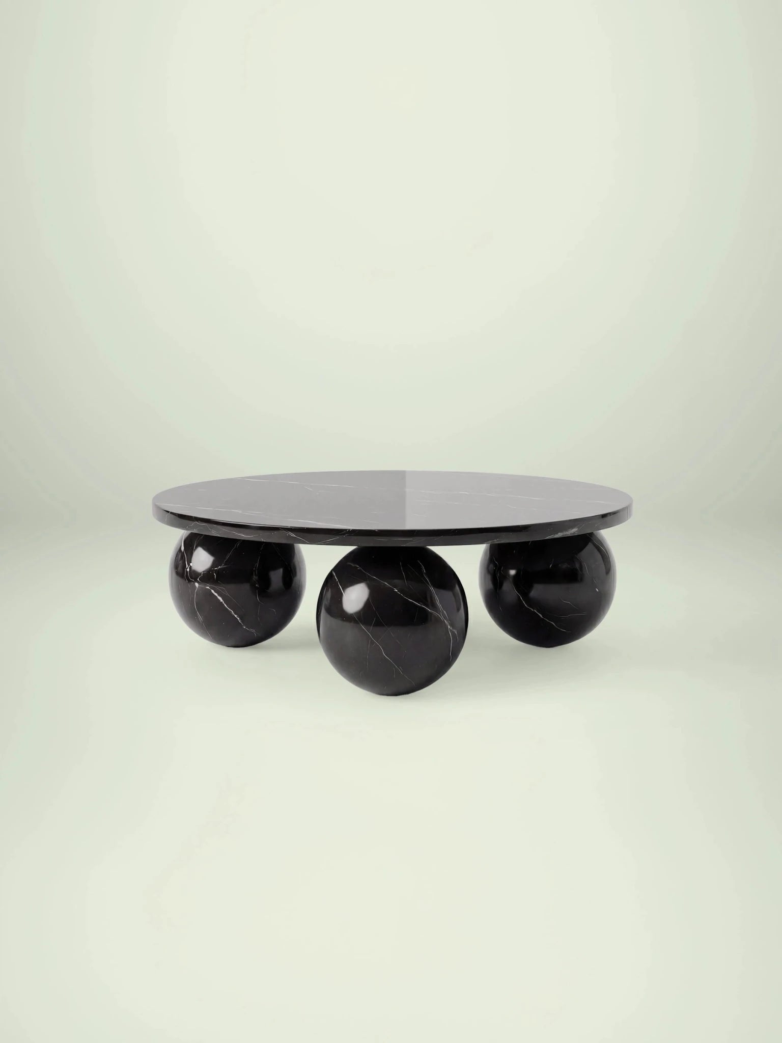 Frontale Studioansicht des Belnor Couchtischs von Menelame. Der runde Tisch aus schwarzem Nero Marquina Marmor ruht auf drei massiven Marmorkugeln, die als Beine fungieren und das skulpturale Design unterstreichen.