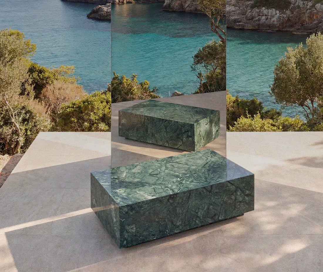 Ein massiver Couchtisch aus grünem Marmor von Menelamé, präsentiert auf einer sonnigen Terrasse mit Meerblick. Die markante Maserung des Natursteins und die künstlerische Spiegelung unterstreichen den luxuriösen Charakter.
