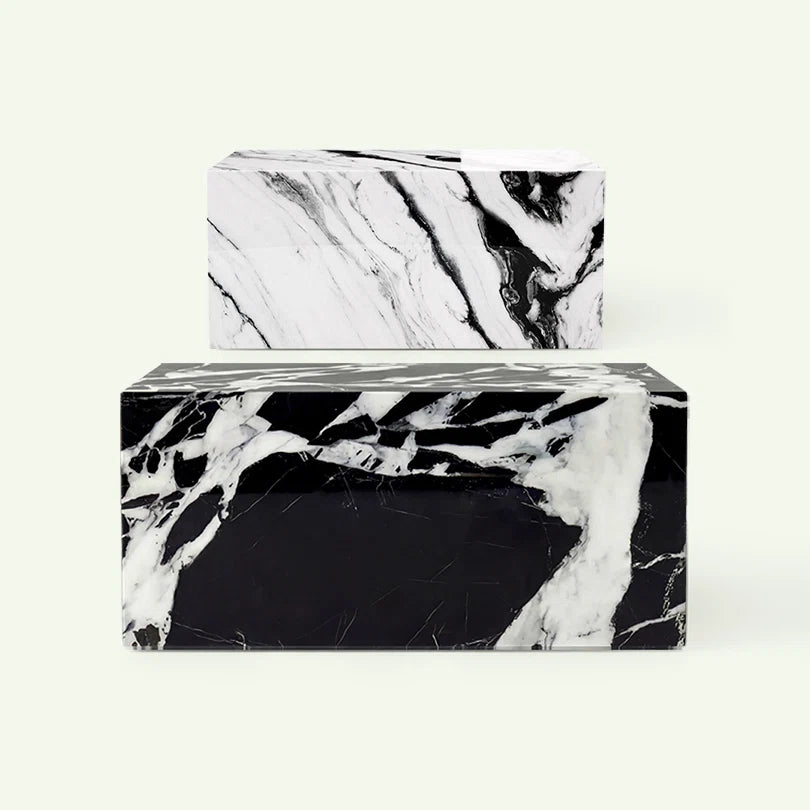 Frontale Übersicht der Lissu Couchtisch-Serie. Im Vordergrund steht die Variante aus tiefschwarzem Grande Antique Marmor, dahinter ist das Modell in Panda White Marmor zur Veranschaulichung der verschiedenen Gesteinsstrukturen zu sehen.