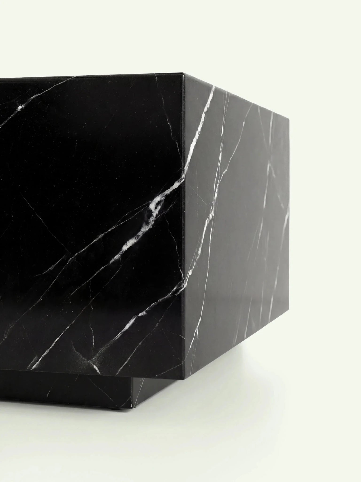 Detailansicht des unteren Bereichs des Madena Couchtischs. Der Fokus liegt auf dem schwebenden Effekt des Sockels und der durchgehenden Marmorierung des schwarzen Nero Marquina Steins an den Seitenwänden.