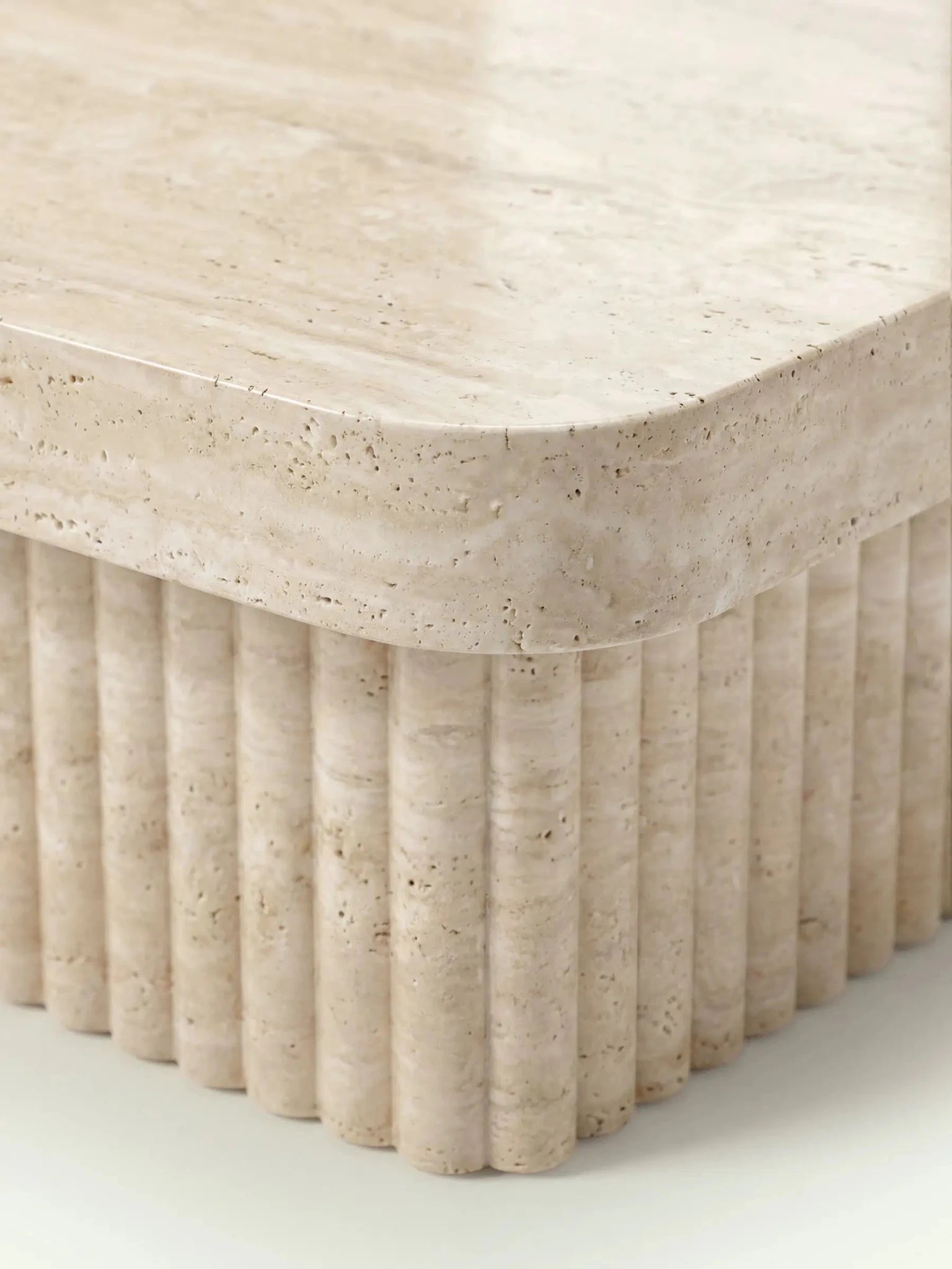 Detailaufnahme der Ecke des Kutio Couchtischs. Die Nahaufnahme zeigt die präzise abgerundete Kante der Travertinplatte und die charakteristischen kleinen Poren des beigen Natursteins.