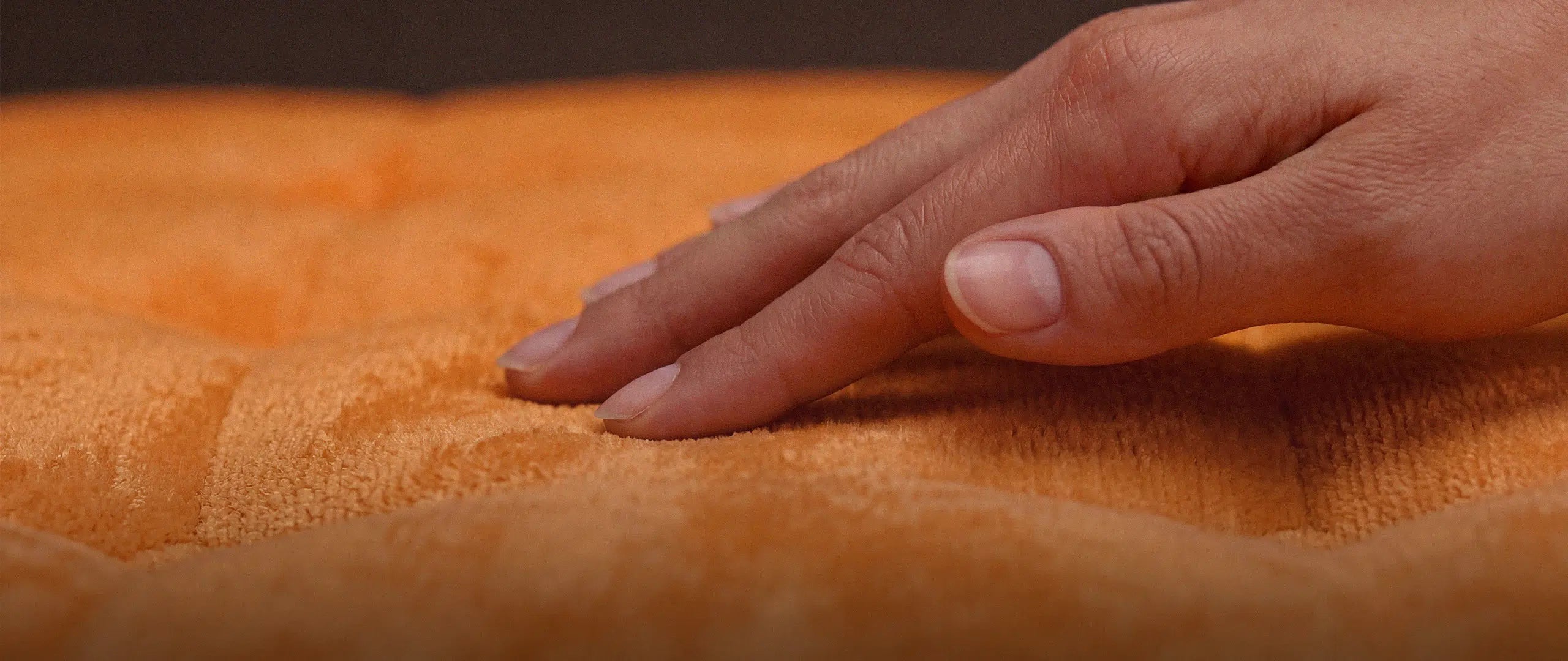 Nahaufnahme einer Hand, die über einen hochwertigen Textilbezug streicht – Symbol für die fachgerechte Pflege und den Werterhalt exklusiver Menelamé Materialien.
