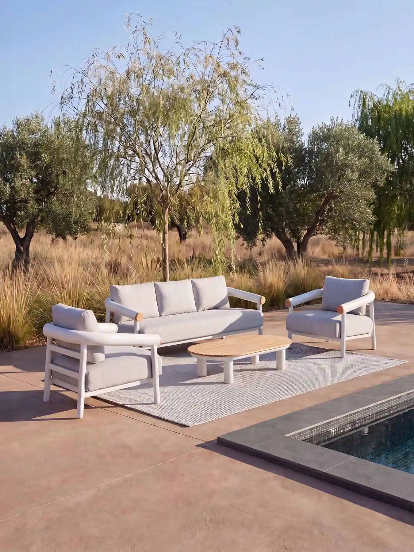 Luxuriöse Menelamé Kanunu Lounge-Ecke im Freien, platziert auf einem Outdoor-Teppich neben einem Swimmingpool.