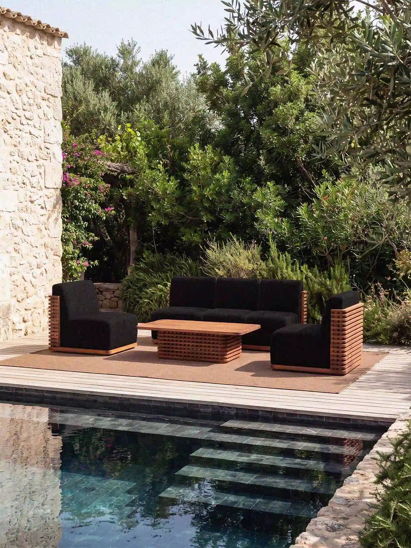 Menelamé Garten-Lounge Puson mit kohlschwarzen Bouclé-Sitzpolstern und massivem Teakholz-Rahmen in einer luxuriösen Pool-Umgebung.