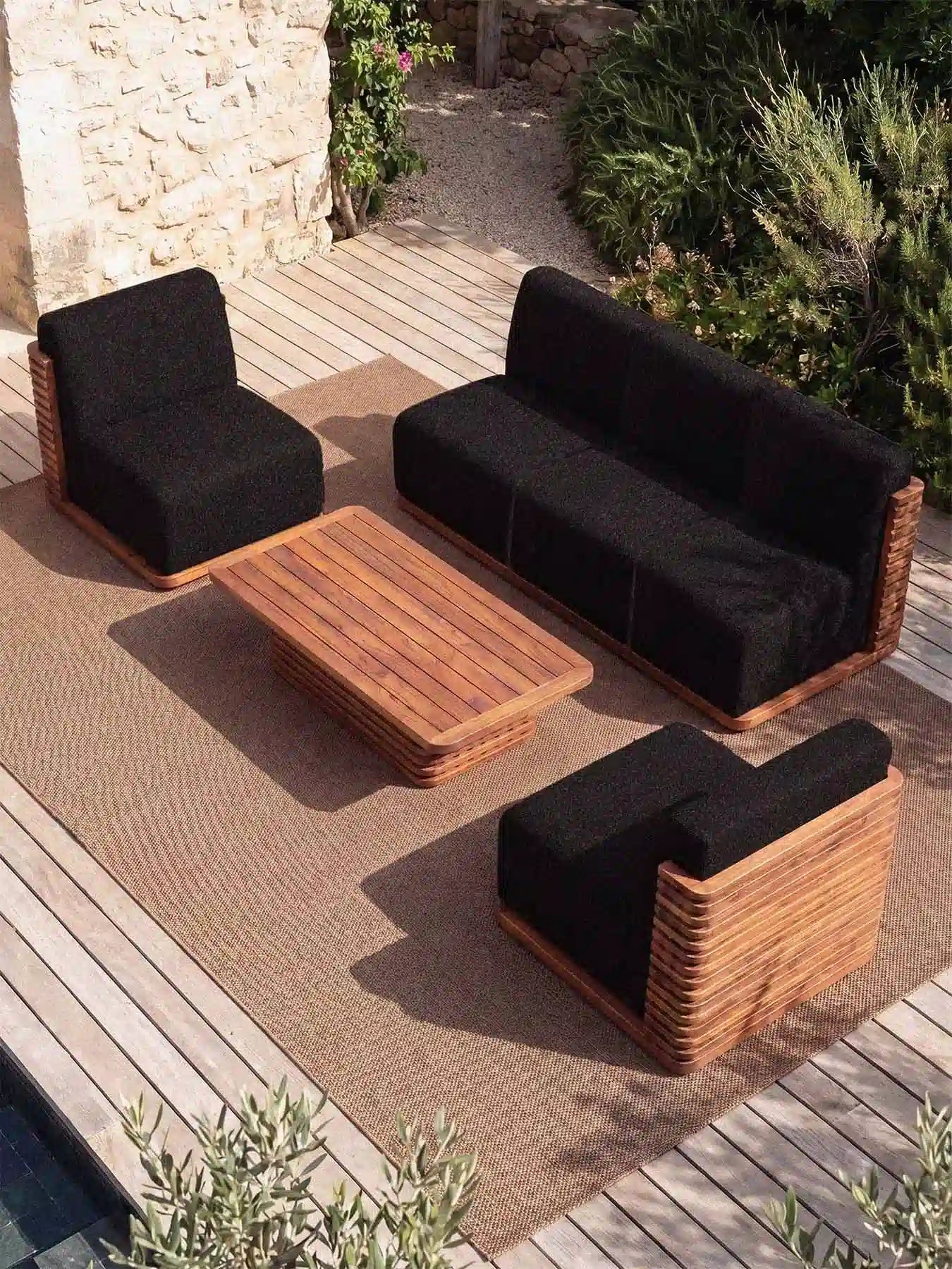 Erhöhte Ansicht der Menelamé Puson Outdoor-Möbel auf einer Terrasse, Kombination aus Teakholz und schwarzen Design-Polstern.