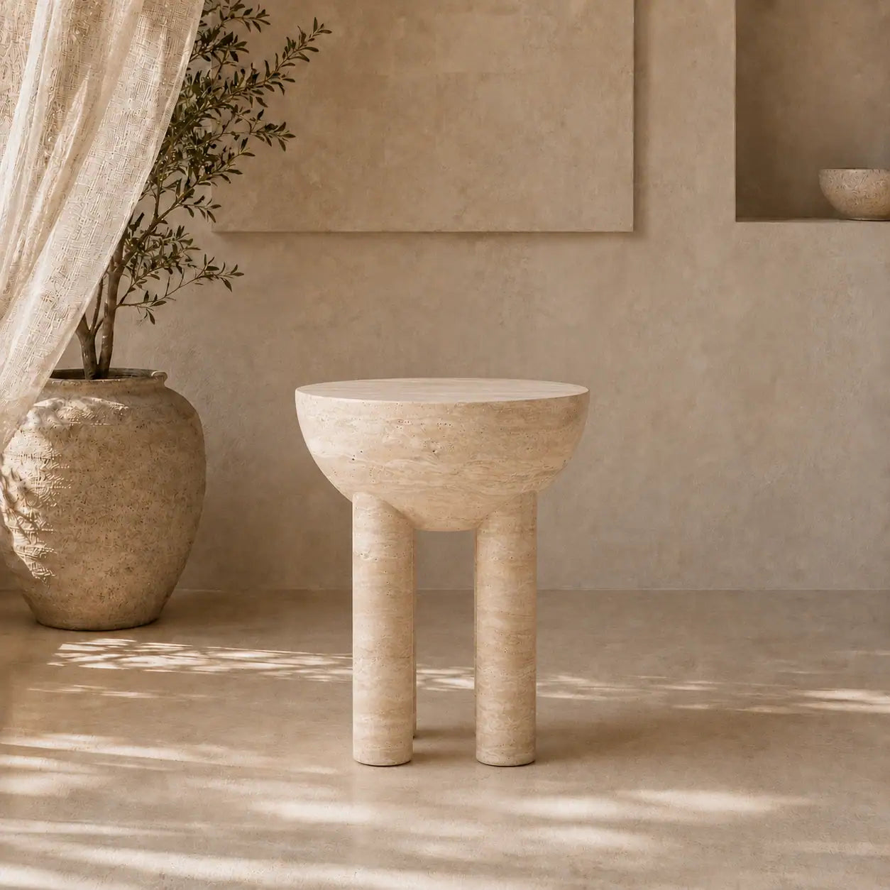 Menelamé Shop by Look: Avantgardistischer, runder Beistelltisch aus cremefarbenem Naturstein mit vier markanten, zylindrischen Beinen neben einer antiken Tonvase.
