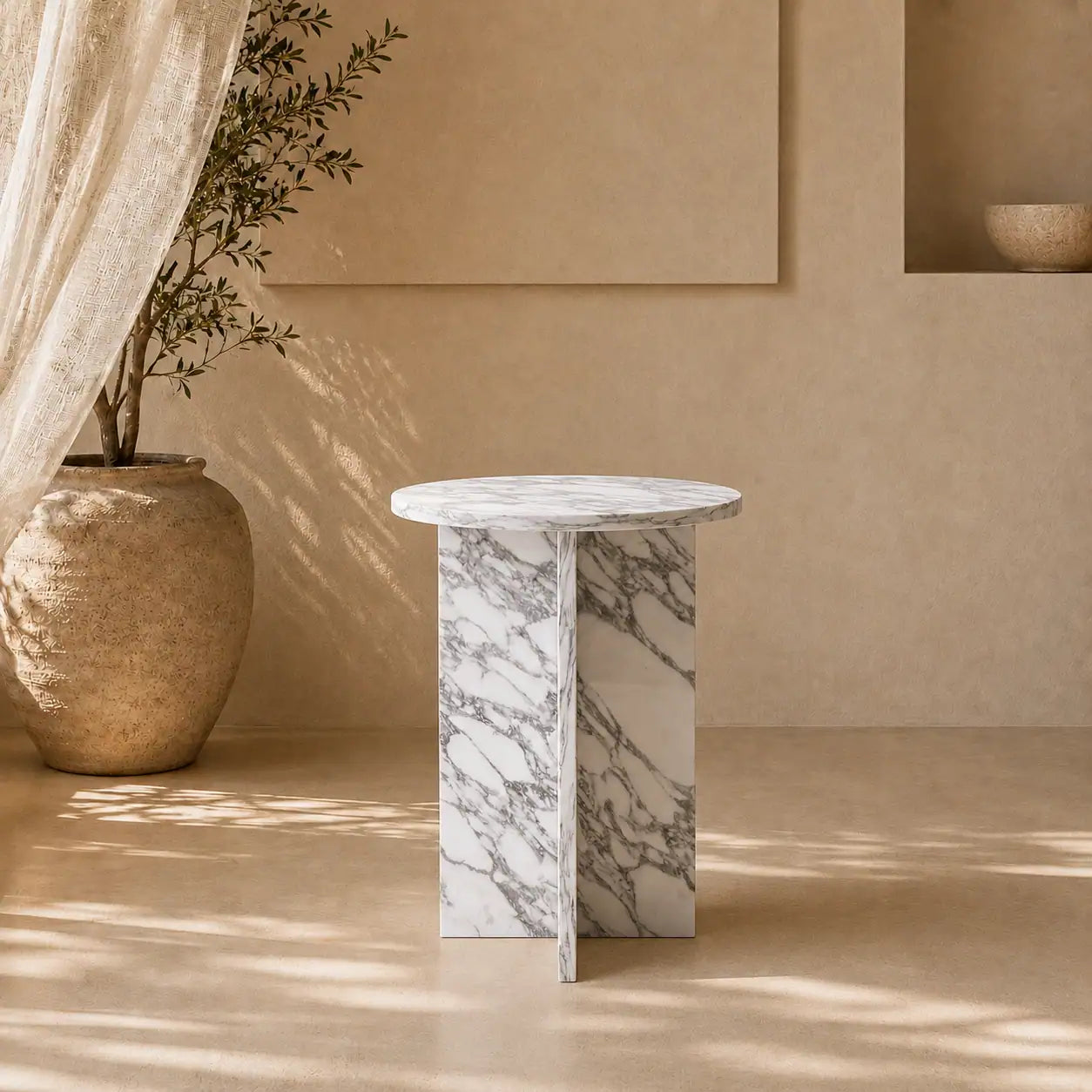Menelamé Shop by Look: Runder, skulpturaler Beistelltisch aus edlem, weiß-grau gemasertem Marmor mit architektonischem Kreuz-Untergestell vor einer minimalistischen Wand.