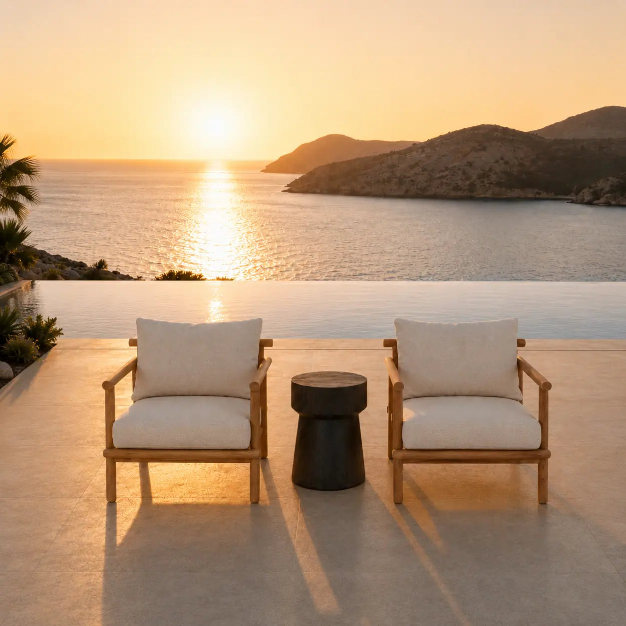Menelamé Shop by Look: Zwei minimalistische Outdoor-Sessel aus edlem Teakholz mit hellem Polster und einem dunklen Beistelltisch direkt am Rand eines Infinity-Pools vor der Meereskulisse.